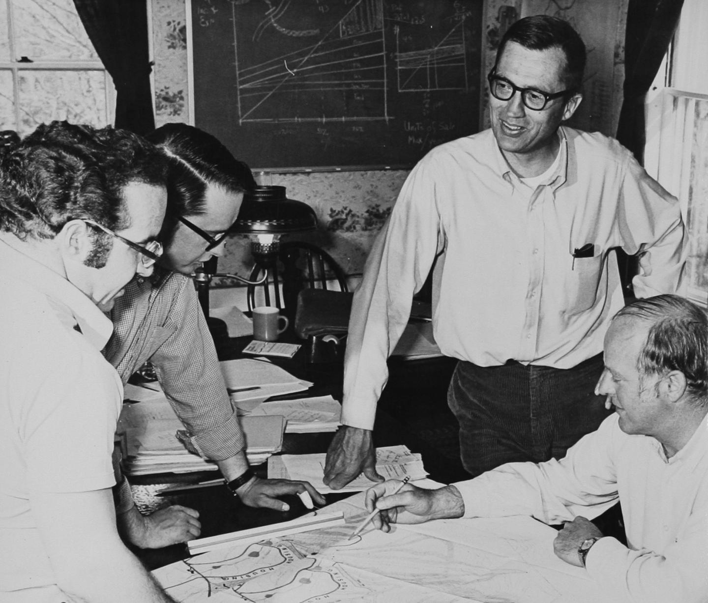 An old photo of a group of people looking at a resort plan