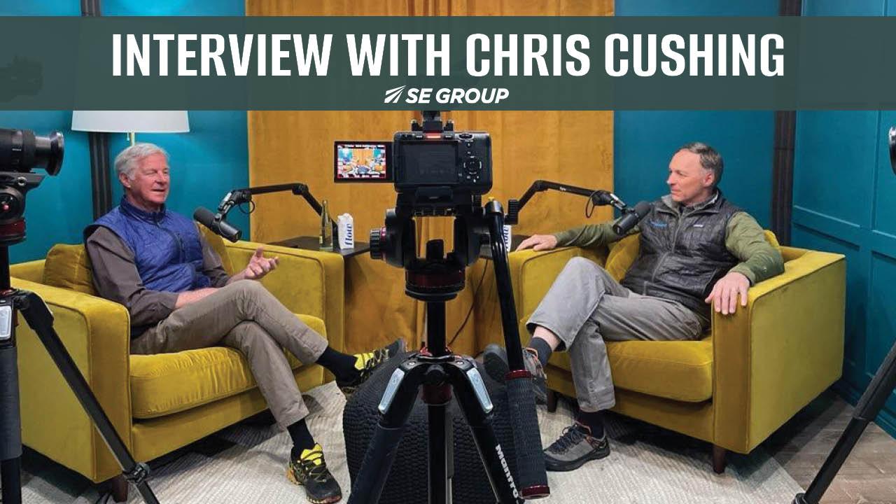 Two men seated on yellow chairs, having a conversation in a studio setting.