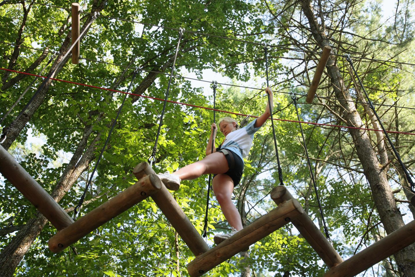 Person climbing a wooden rope course in a forest setting.