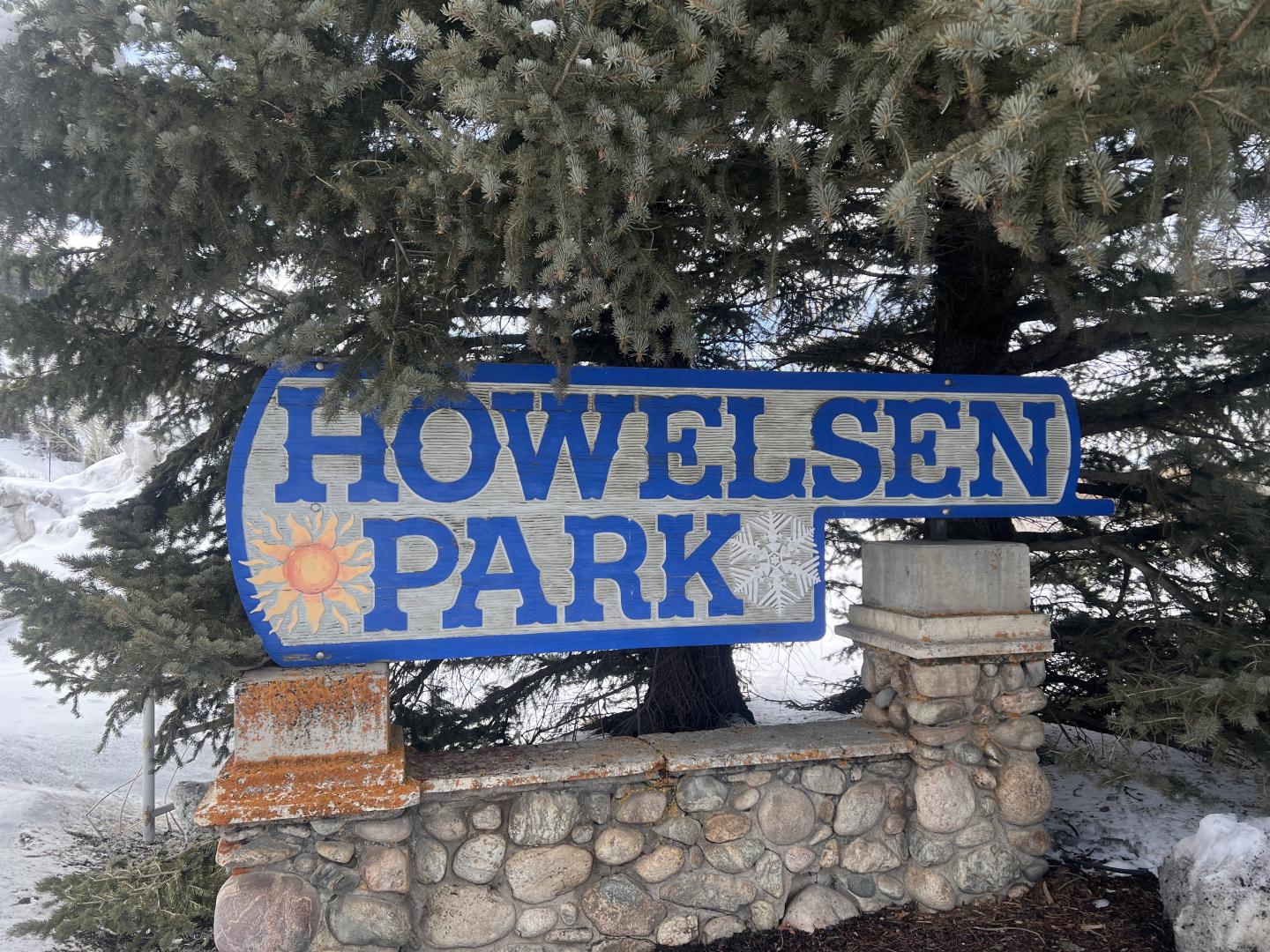 Howelsen Park sign with a sun icon, surrounded by snowy trees.
