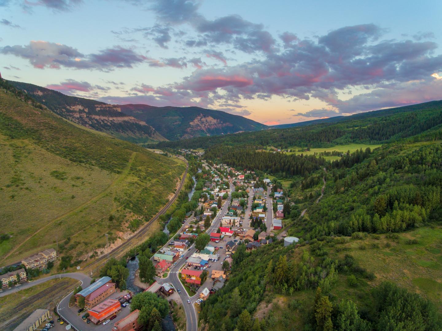 Aerial view of a small town in a valley at sunset, surrounded by lush green hills.
