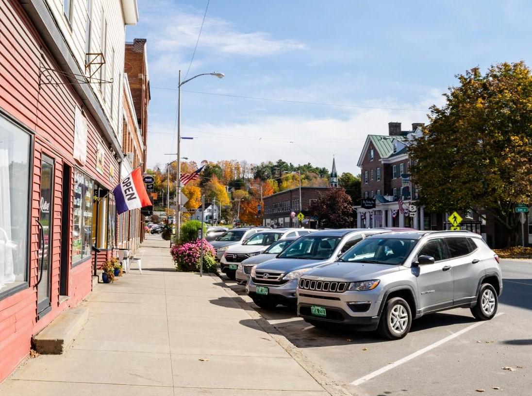 Small town street with parked cars and autumn trees.