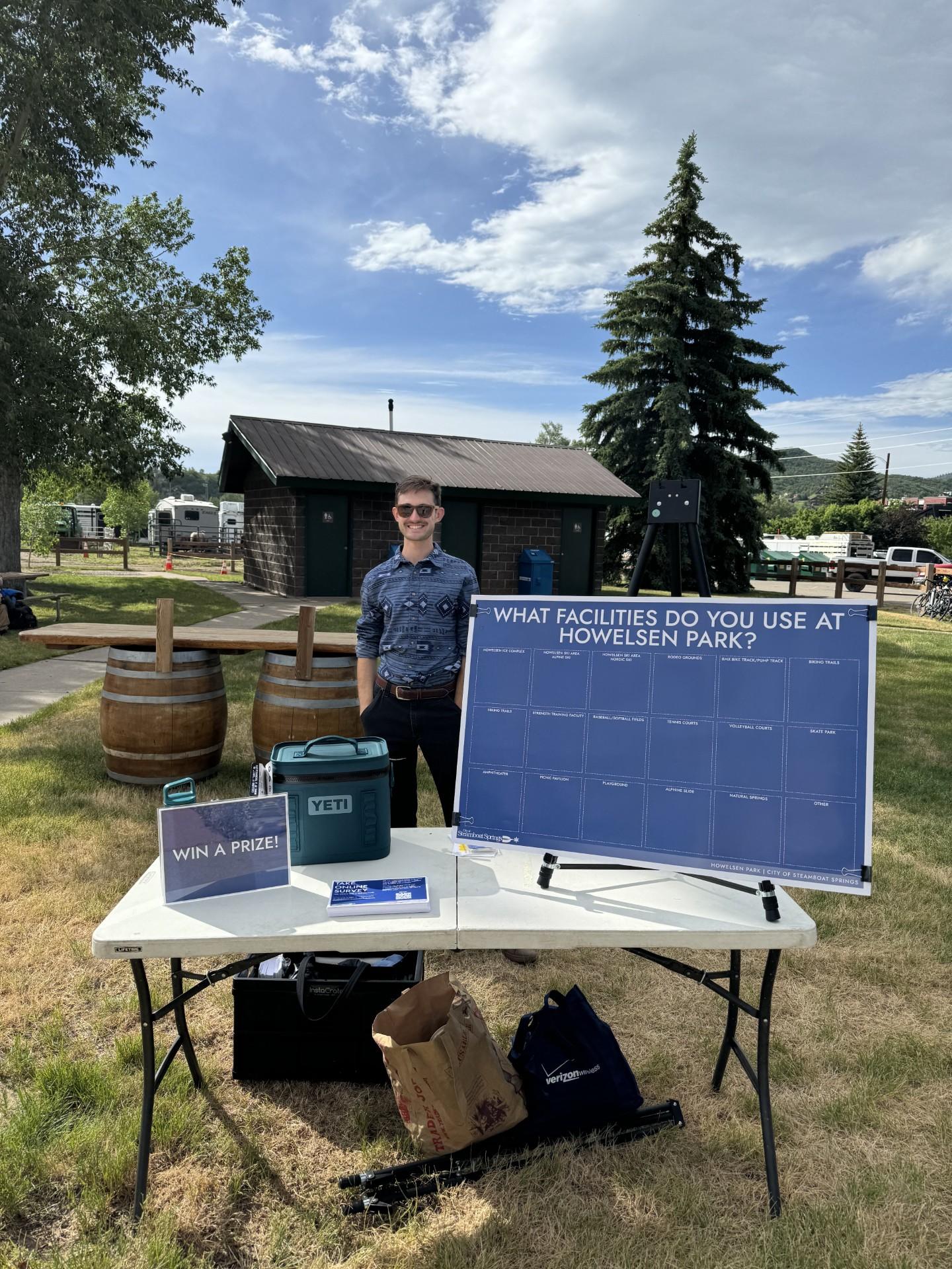 Outdoor event booth with a man standing behind a table under a cloudy sky.
