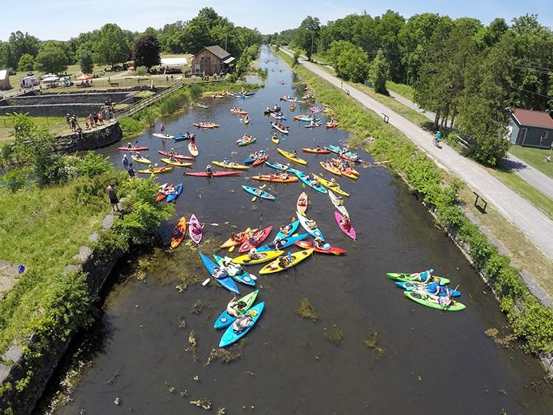 Colorful kayaks crowd a narrow canal on a sunny day.