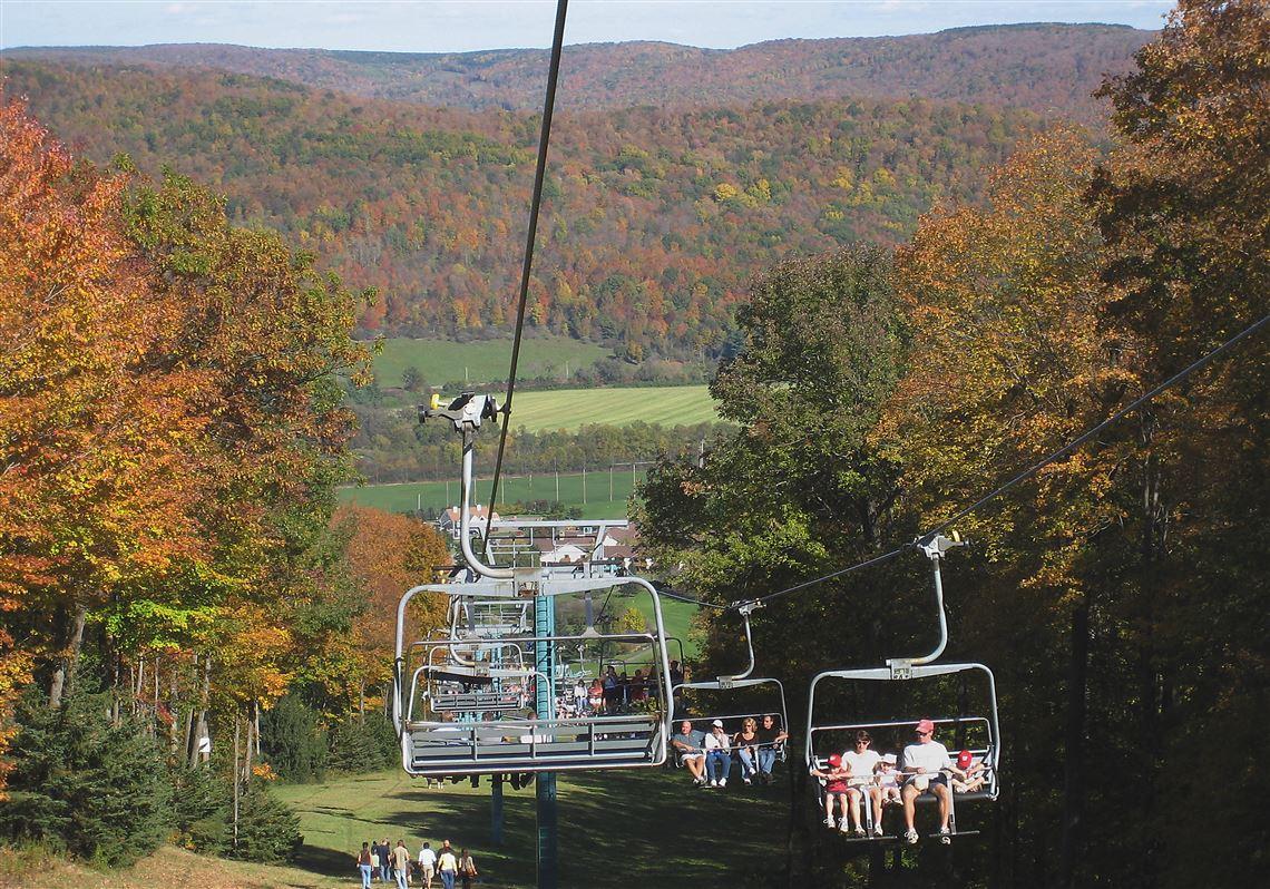 Ski lift in autumn landscape with colorful foliage and distant hills.