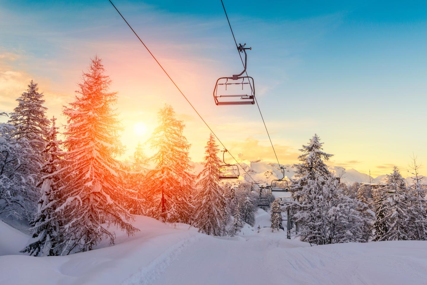 Ski lift over snowy landscape at sunrise, with snow-covered trees and vibrant sky.