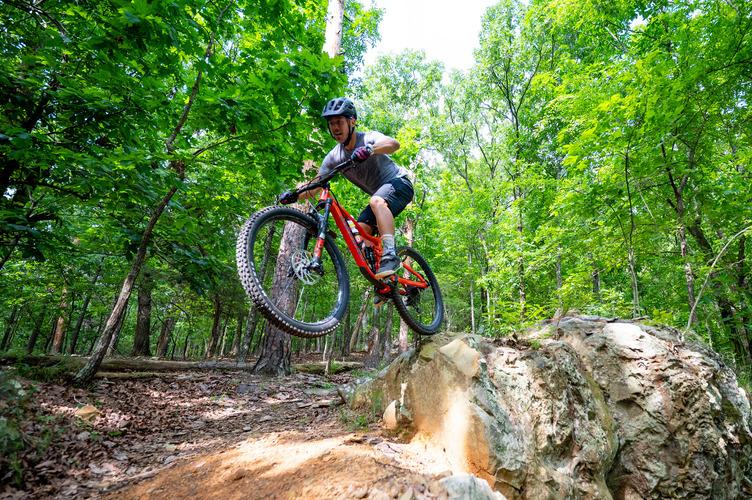 Mountain biker jumps over a rock in a forest setting.