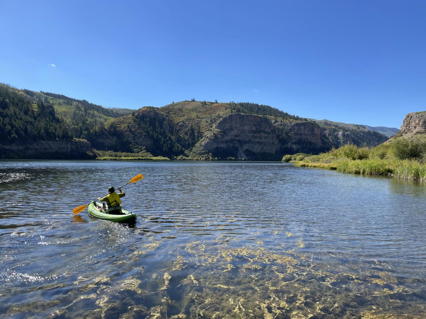 Kayaker on a lake surrounded by hills and greenery under a clear blue sky.