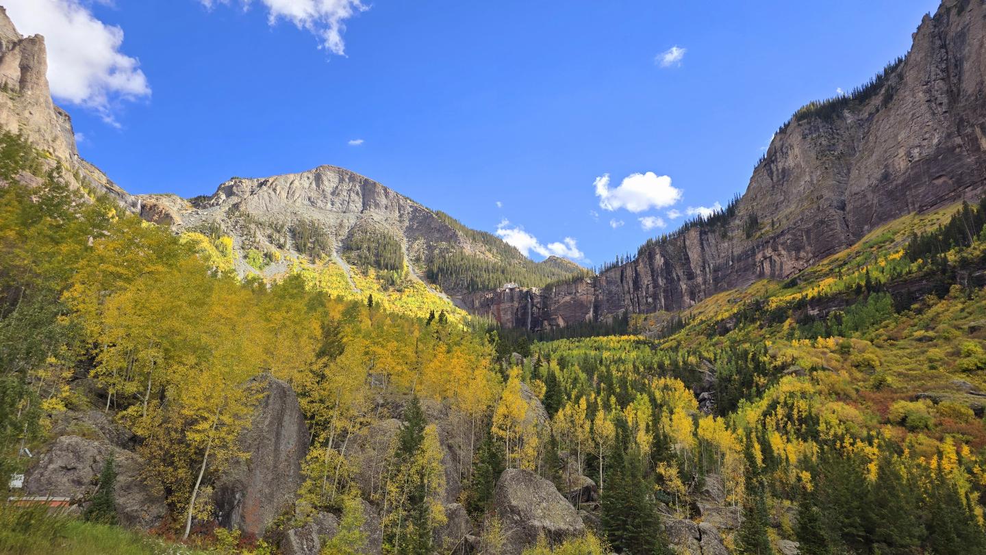 Mountain landscape with autumn foliage under a bright blue sky.