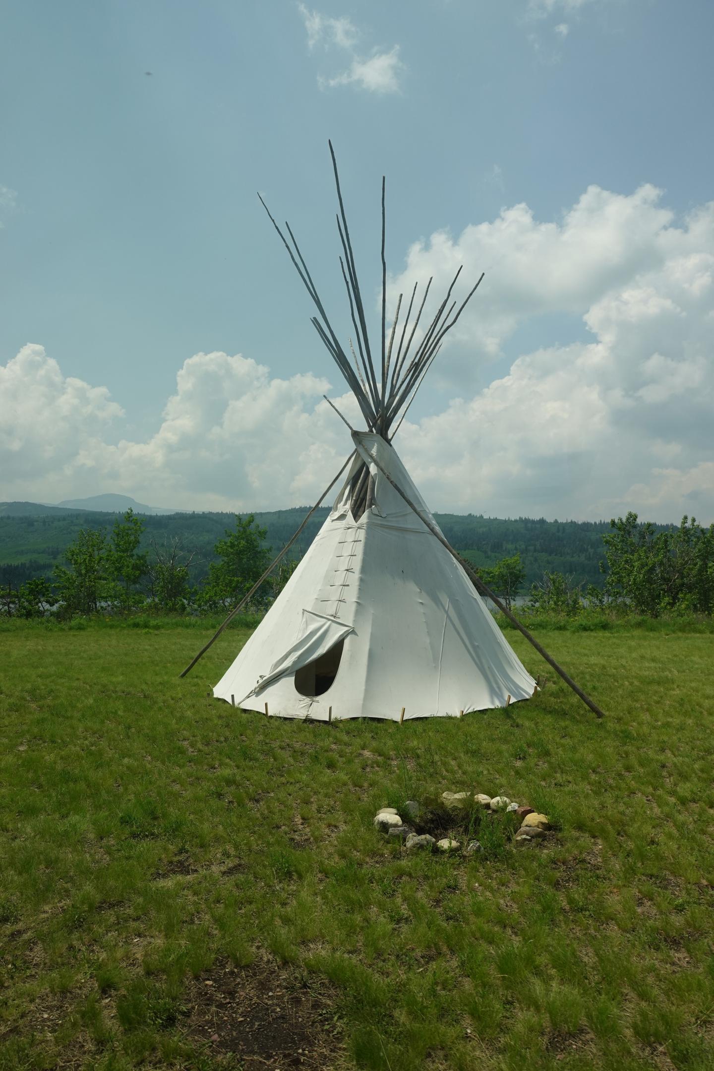 White tipi on grassy field under blue sky with fluffy clouds.