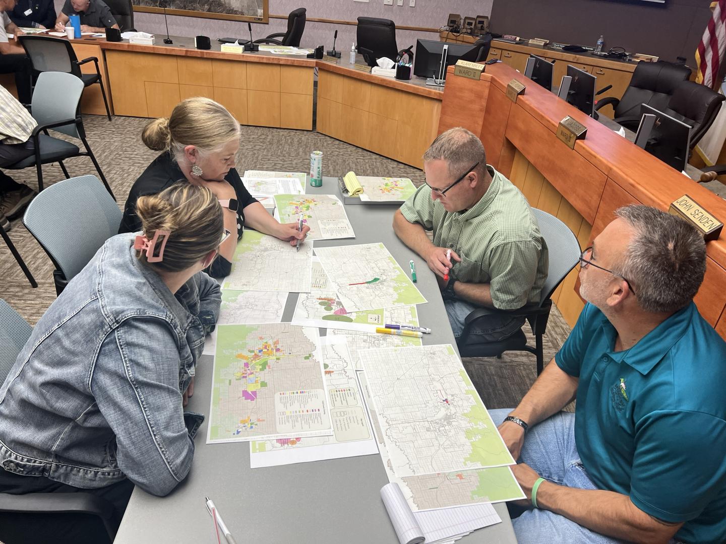 Four people sitting at a table, examining maps in a conference room.
