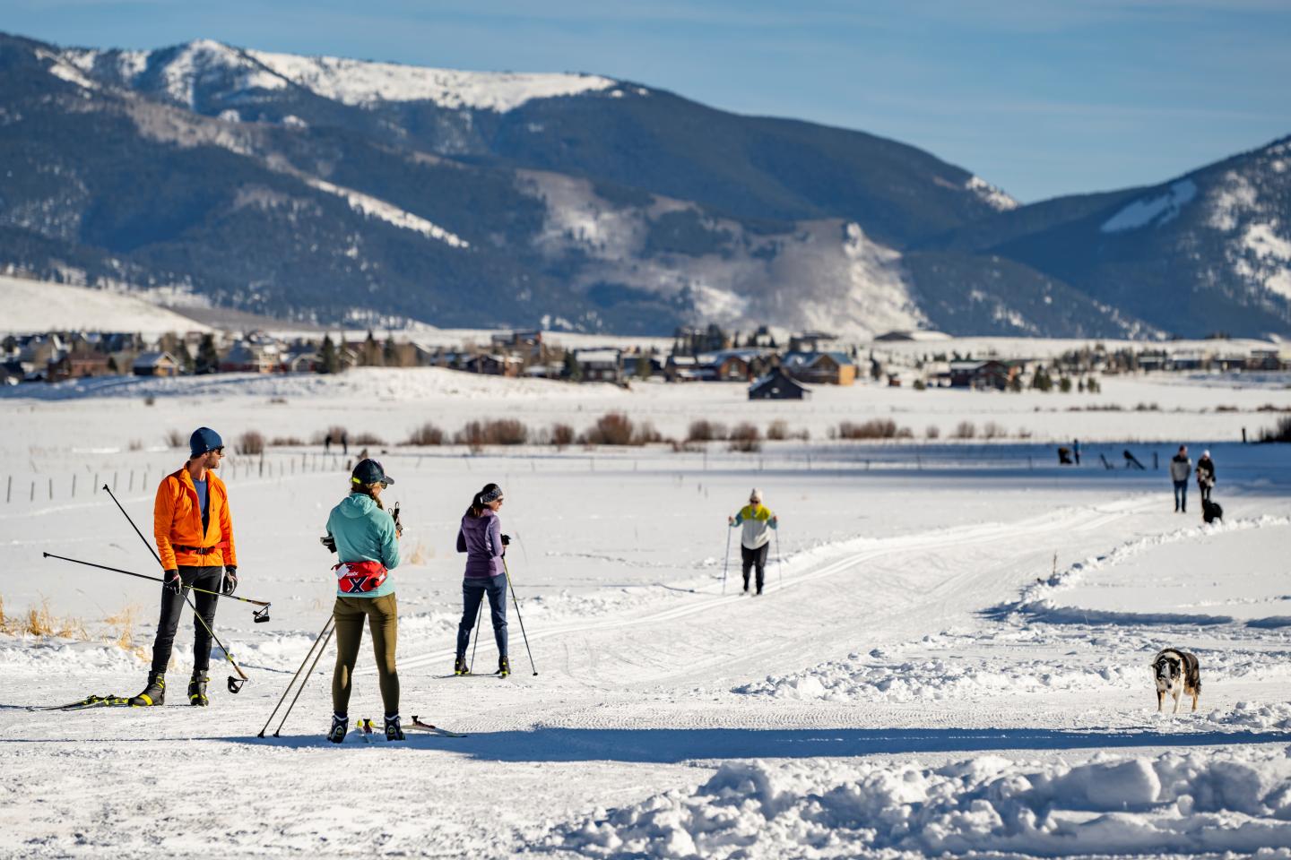 Cross-country skiers on a snow trail with mountains in the background.