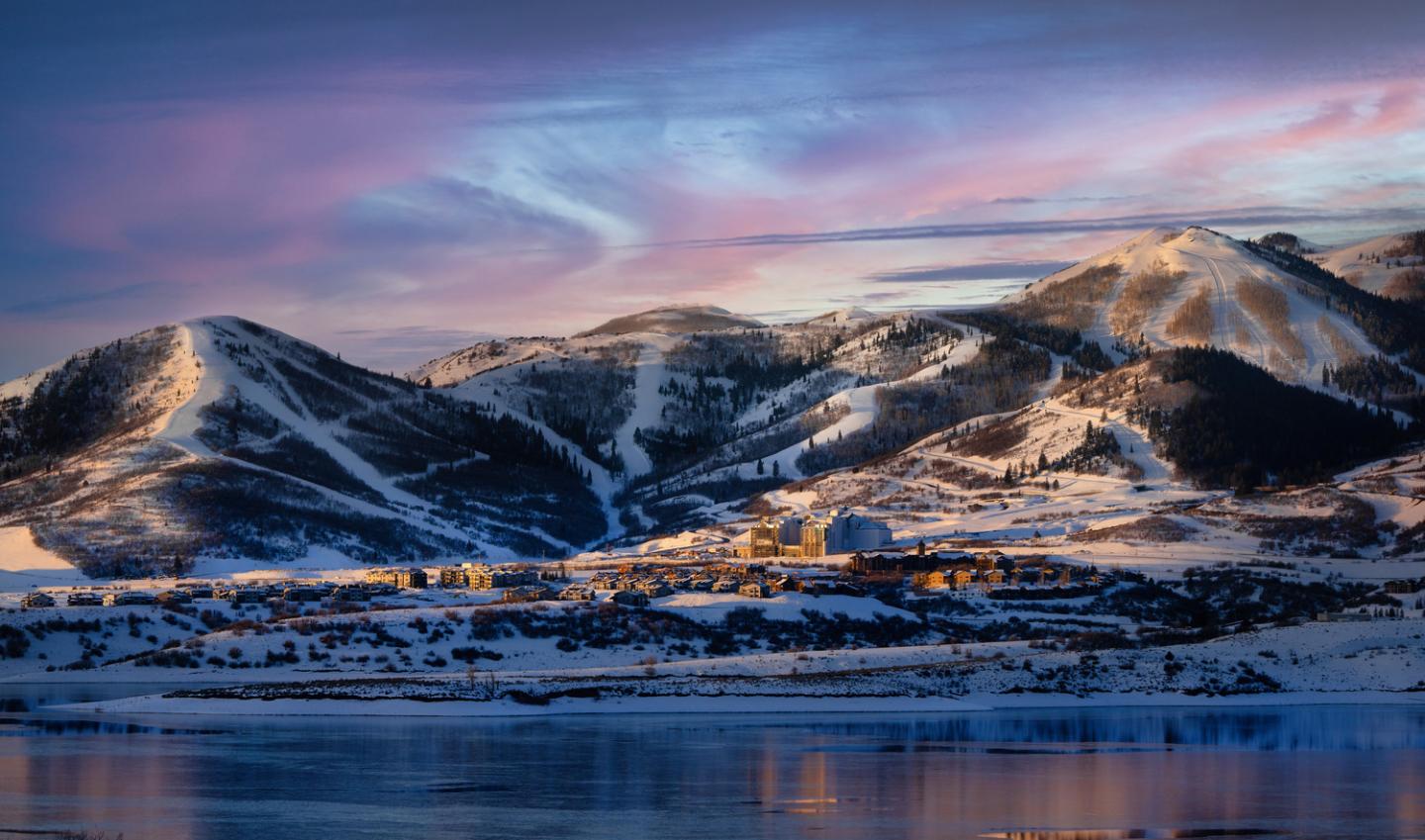 Snowy mountains at sunset with a town in the foreground.