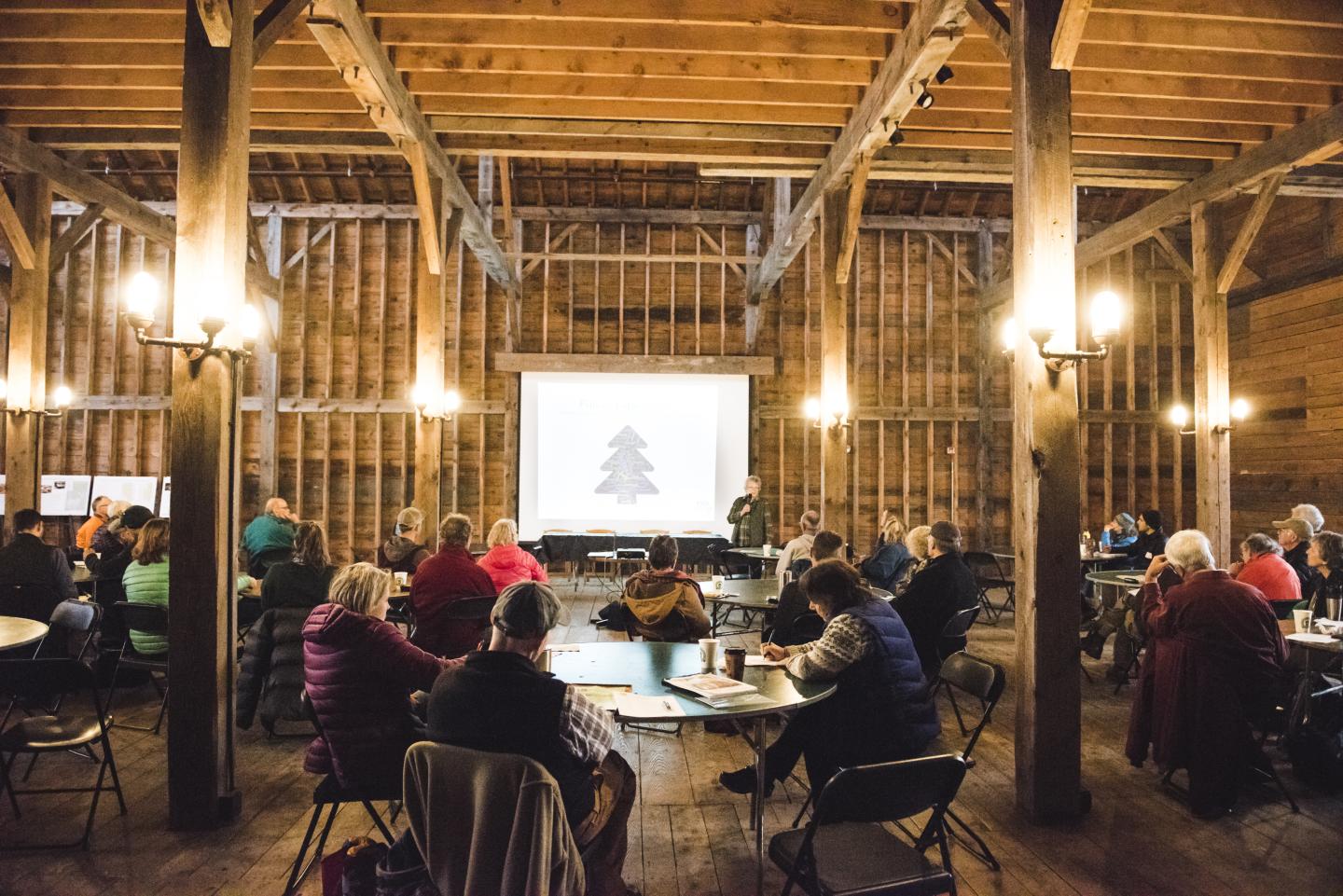 Cozy barn meeting with people seated around tables, viewing a projected screen.
