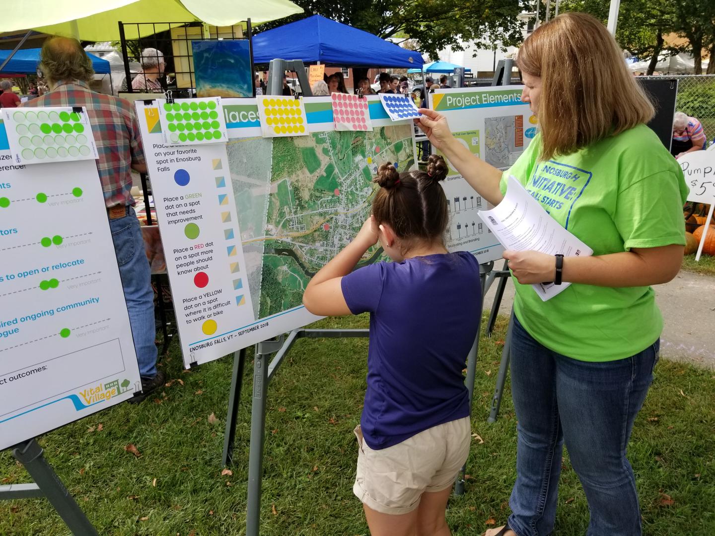 Two people examine large maps at an outdoor booth.