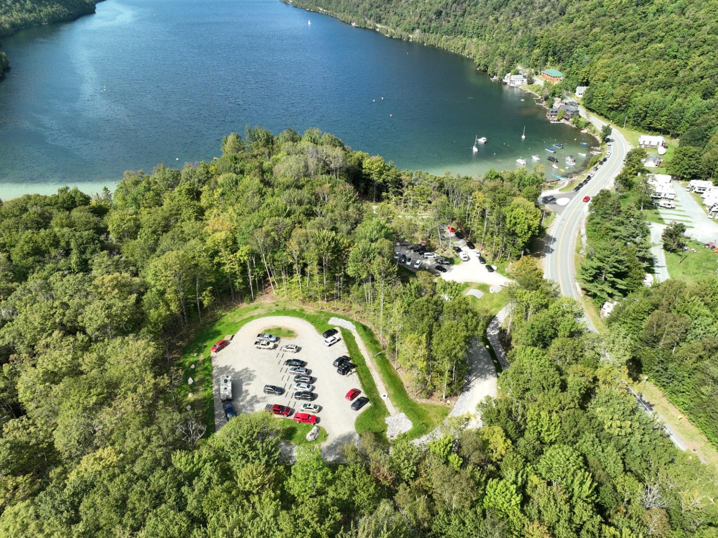 Arial view of a lake, trees, and a nearby parking area with cars.