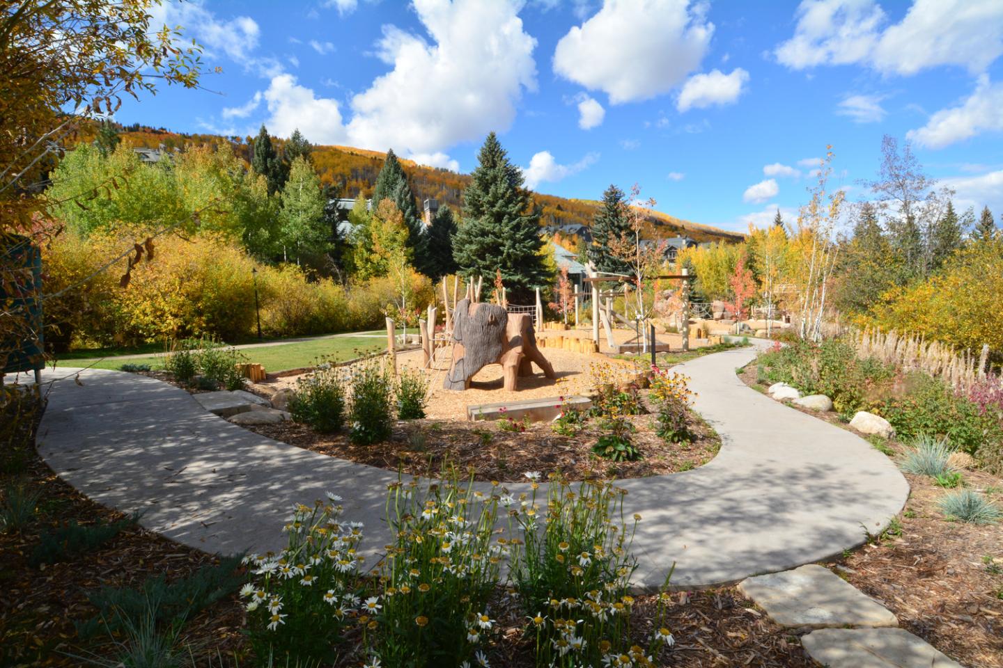 Playground with trees and winding path under a blue sky with clouds.