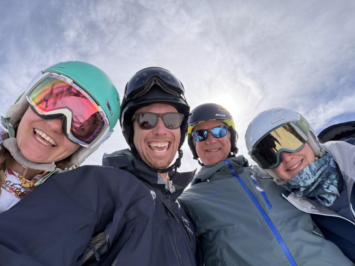 Four smiling people in ski gear on a snowy day, sun shining behind them.