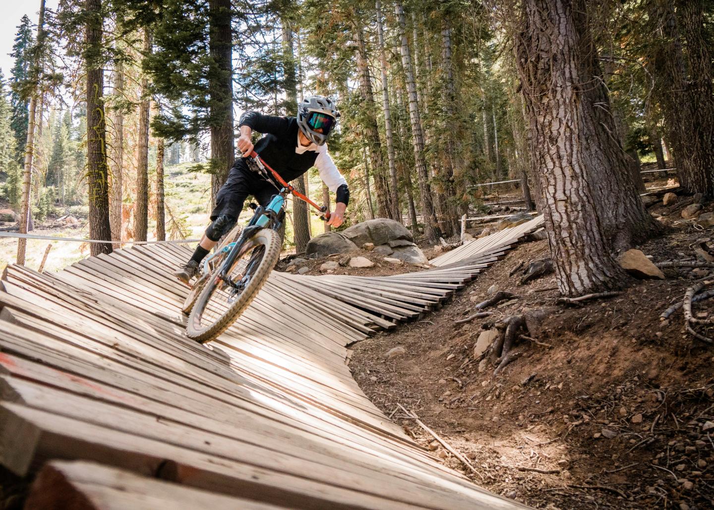 Mountain biker riding over a wooden trail berm in a forest.